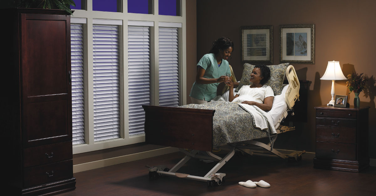 A woman in an adjustable bed with the back raised being attended on by a nurse.